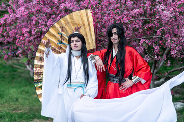 A male cosplayer with long hair in a kimono against a sakura background