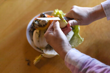 hands peeling an apple over a food waste container