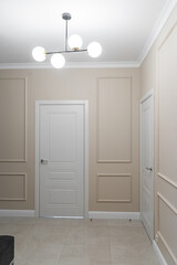 stylish corridor design in flat, apartment, hotel room or house. Light walls and floor. Light wooden doors, beautiful chandeliers on ceiling. Soft lighting. Light furniture and an entrance hall.