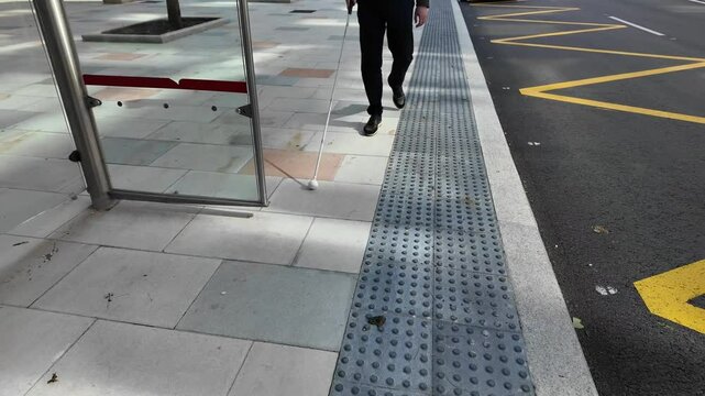 Blind person sitting on the bench of the bus stop using his guide cane