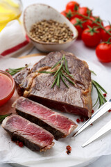 Pieces of delicious beef meat, spices, tomatoes and fork on table, closeup