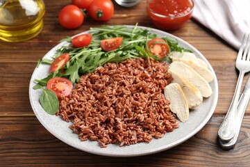 Delicious brown rice with chicken and salad served on wooden table, closeup