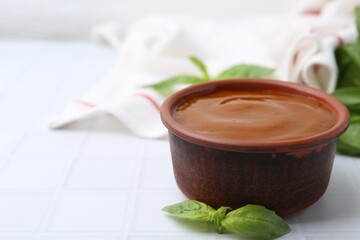 Tasty curry sauce and basil leaves on white tiled table, closeup. Space for text