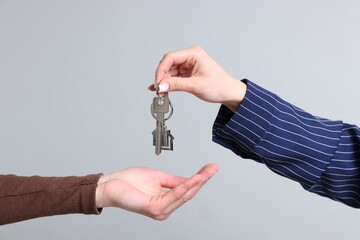 Real estate agent giving house key to new owner on gray background, closeup