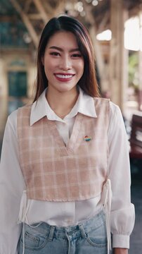 Portrait of Asian transwoman with rainbow heart pin on chest waiting for train at station. Brunette lesbian expresses LGBT pride travelling by railway transport. Vertical shot