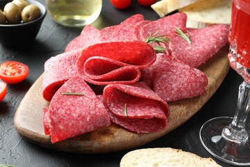Slices of delicious sausage with rosemary served on black table, closeup
