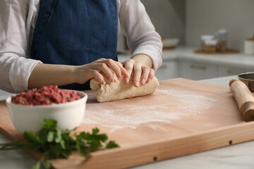 Making khinkali. Woman kneading dough at table in kitchen, closeup
