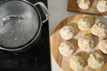 Cooktop with pot and uncooked khinkali on countertop in kitchen, top view
