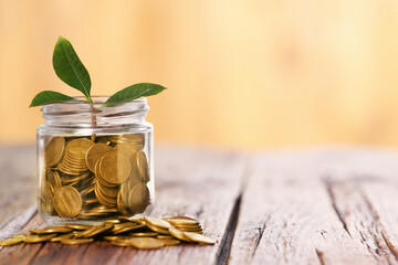 Investment concept. Glass jar with coins and sprout on wooden table against blurred orange...