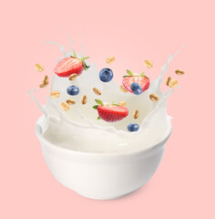 Oat flakes with fresh berries and milk splashing out from bowl on pink background