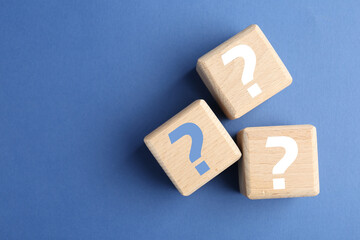Wooden cubes with question marks on blue background, top view. Space for text
