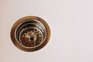 Drain with metal strainer on white surface in modern kitchen