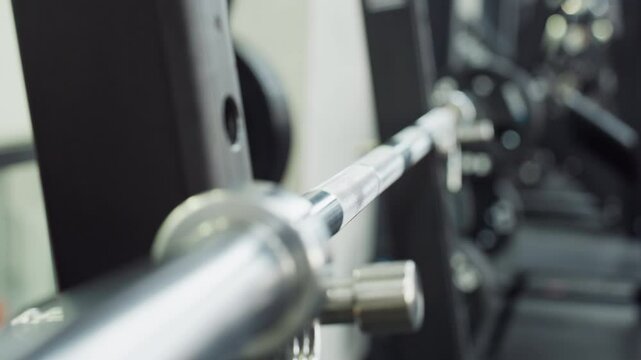 Chrome bar secured on smith machine glides between safety hooks beside stacked black weight plates and metal bench in modern gym strength zone ready for heavy squat press workout