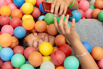 Young girl using smartphone while relaxing in colorful ball pit