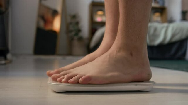 Medium closeup of unrecognizable barefoot man stepping on scale to check weight