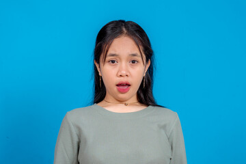 Fototapeta premium Portrait of a young Asian woman expressing shock and surprise with wide eyes and open mouth. Isolated on blue background. Concept of disbelief, astonishment, and reaction.