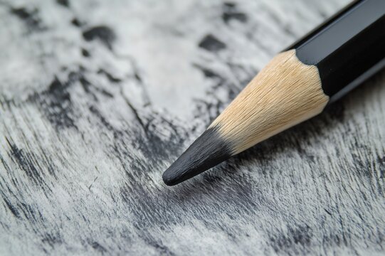 Close up of a black charcoal pencil creating parallel strokes on textured drawing paper, highlighting the artistic process and texture details