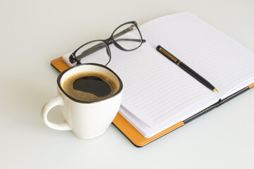 Office supplies. A notepad for notes, a pen, and a cup of coffee on the desk.