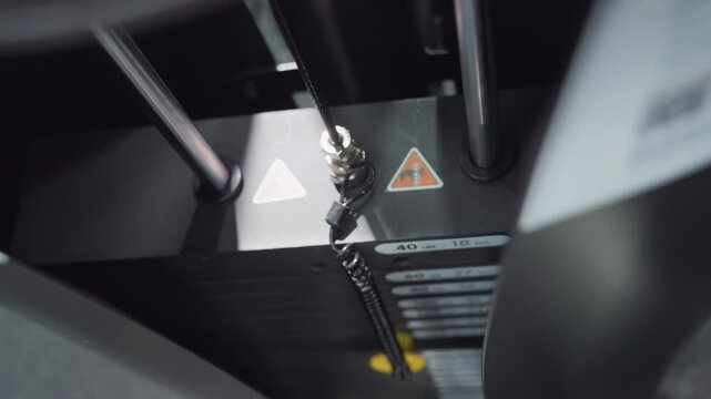Close up of weight stack moving on gym machine showing pin shifting between plates labeled in pounds and kilograms under bright gym lighting with cable coil and selector pin adjusting resistance