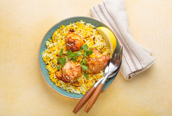 Delicious indian chicken biryani with chicken, garnished with fresh cilantro and lemon, in a bowl on a beige table, accompanied by cutlery. Authentic dish of India