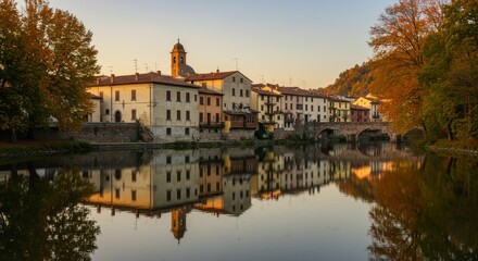 Fototapeta premium Charming River Town at Sunset - Picturesque autumnal scene of a river town reflecting in calm water at sunset. Historic buildings line the riverbank