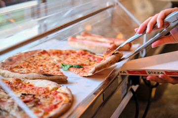 Chef taking pizza slice with tongs from restaurant display case