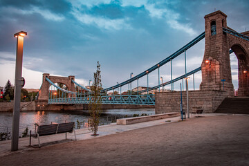 Fototapeta premium A beautiful urban bridge over the river and a quiet, deserted waterfront with soft evening lighting.