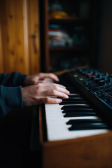 Fototapeta premium Hands are playing on a keyboard instrument with a wooden frame in a cozy interior setting. Concept: music creation, home studio, creativity