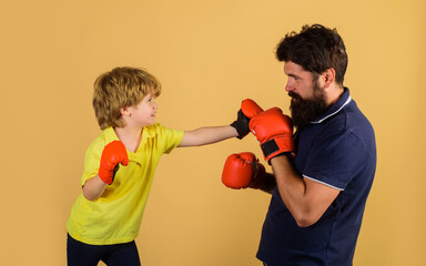 Kid boxer practicing punches with coach at boxing training. Little son doing boxing exercises with father in gym. Child and coach in boxing ring. Boy and trainer in boxing gloves. Future champion.