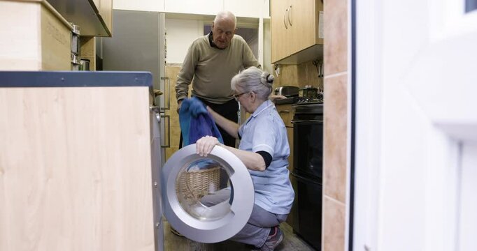 Cleaner, cleaning and senior couple doing laundry, loading clothes and housework in washing machine. Working, help and elderly man and woman talking and sorting clothing for chores and housekeeping - Powered by Adobe