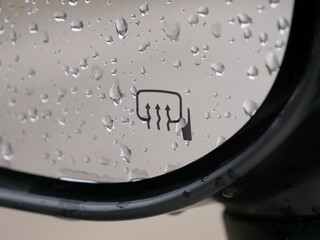 Raindrops covering a car's side mirror with the heating symbol, ensuring clear visibility during bad weather conditions