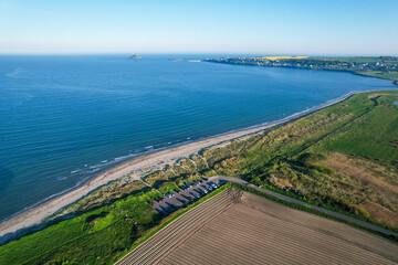 Aerial view of Ballynamona Beach and Ballycotton Bay, County Cork, Ireland, featuring a sandy shoreline, green fields, parked cars, and the iconic Ballycotton  on a clear summer day.