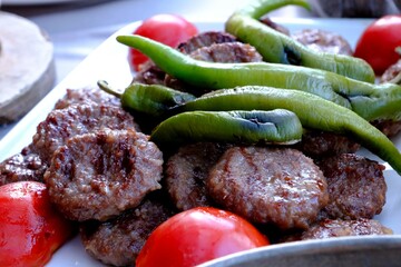 Traditional Turkish cuisine delicacy meatballs close-up. Roasted green peppers and tomatoes on top. Mom's meatball recipe. Grilled meatballs with beef. Dinner at a meatball restaurant. Food industry.
