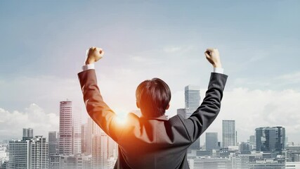 Businessman celebrating success with arms raised against city skyline at sunset