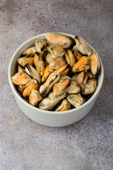 Cleaned boiled mussels in a bowl on a dark background, top view.