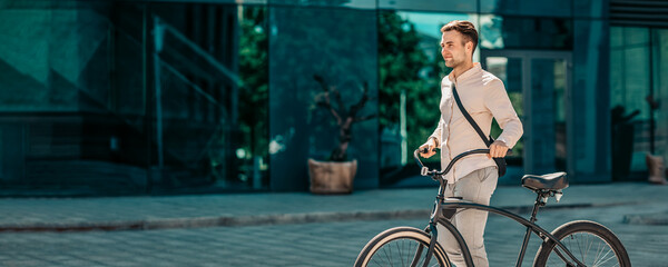 A young man casually rides his bike down a sunny city street, embodying a millennial lifestyle. He wears stylish attire and enjoys the vibrant urban environment around him, copy space