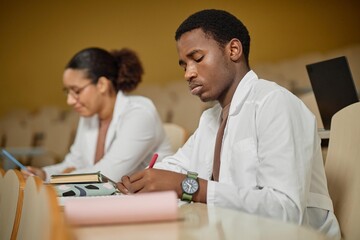 Side view portrait of young African American man as med student taking notes during lecture in college or university