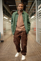 Full length portrait of African American man walking towards camera in college hallway