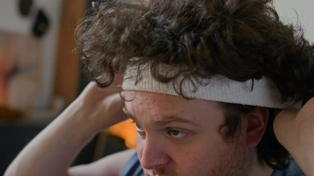 Stocky Caucasian man in sportswear adjusting unruly curly hair and white headband before workout