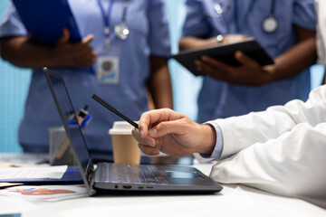 Doctor expert examining radiography scan results and healthcare records on laptop, discussing with team about potential treatment. Medics collaborating on disease prevention. Close up.
