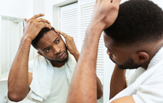 Hairloss concept. Young african man checking for thinning hair in mirror at bathroom