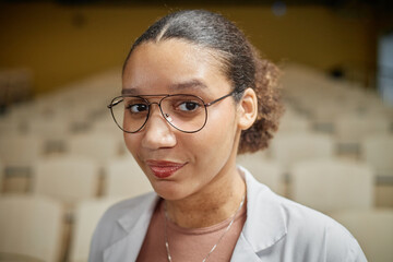 Obraz premium Vertical portrait of young African American med student holding laptop and notebook while standing in empty college lecture hall, copy space