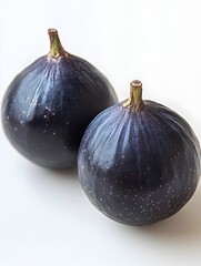 Two ripe dark purple figs sit closely together on a bright white background showcasing their rich color and texture.