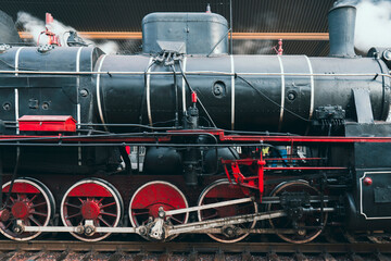 Obraz premium Close-up side view of a powerful vintage steam train locomotive. Showcases the large red wheels and complex mechanical engineering