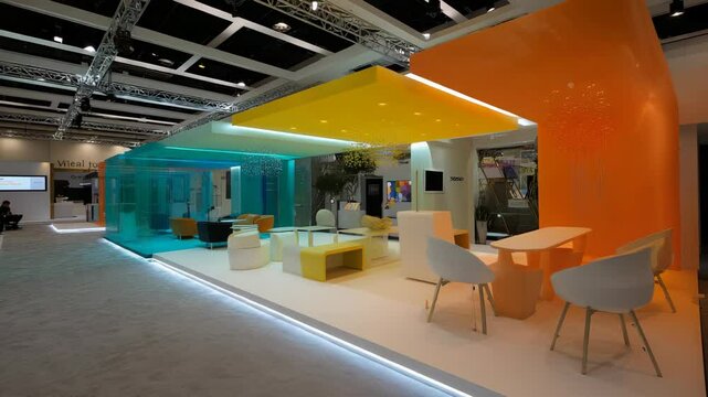 Colorful trade show exhibit interior, modern design with orange, yellow and blue, seating area and meeting spaces for business events.
