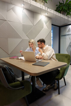 Two individuals work together in a modern office space with a laptop