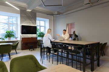 Two coworkers having a discussion in an office setting with modern furnishings.