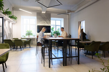 Contemporary office space featuring green chairs, plants, and individuals engaged in work projects