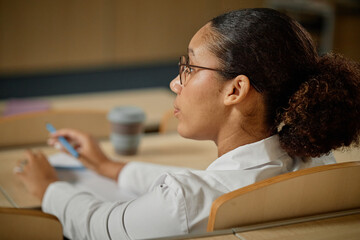 Side view closeup portrait of young med student listening to lecture in college and holding pen,...