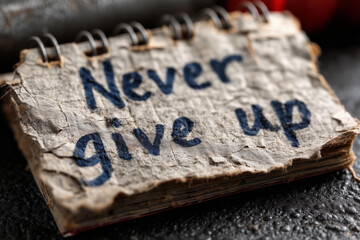 Obraz premium On a weathered surface, a torn notebook page showcases the bold, handwritten message Never give up